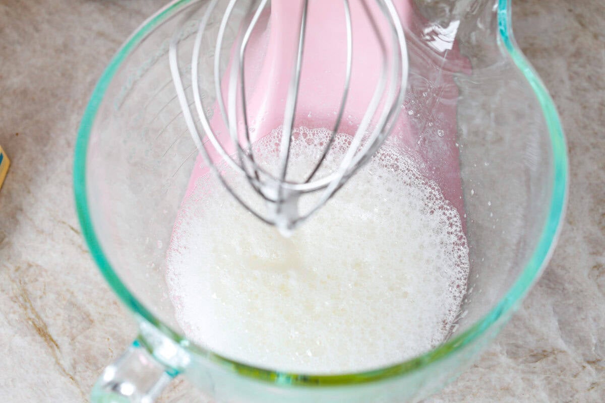 Overhead shot of stand mixer with foamy egg whites in bowl. 