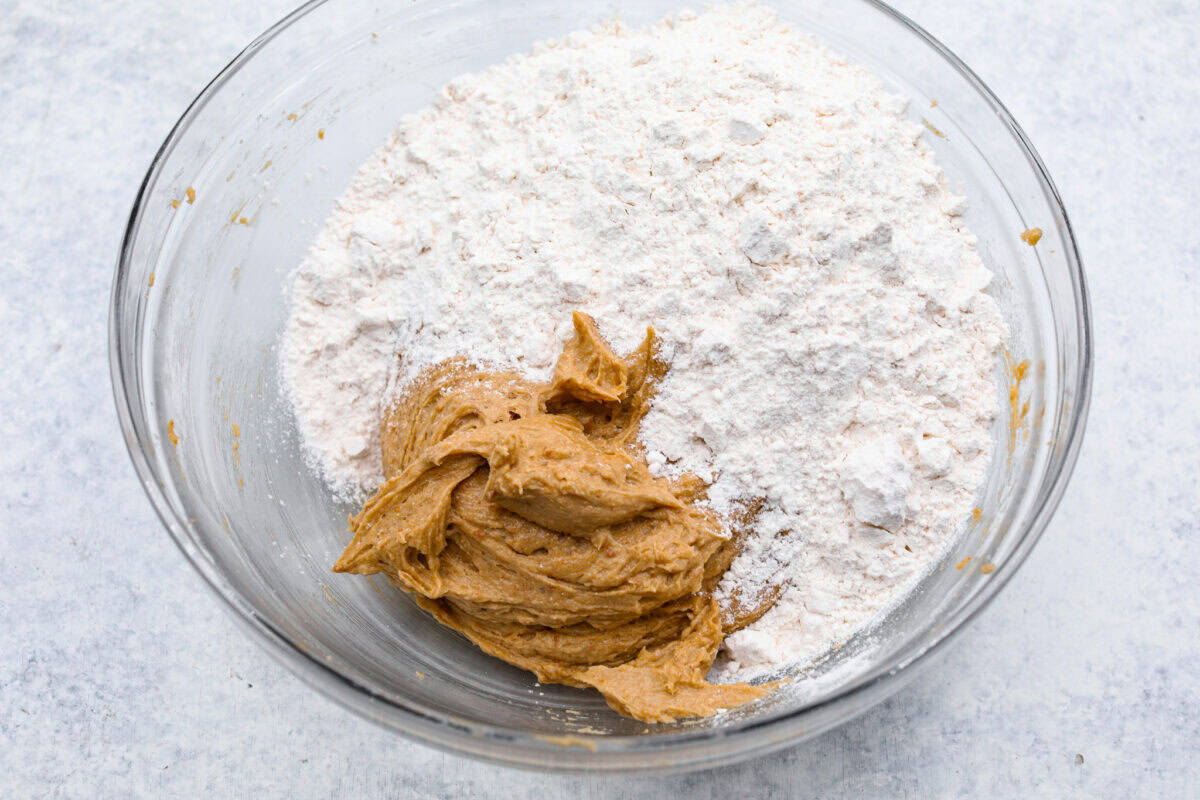 Overhead shot of bowl of cookie dough with dry ingredients on top. 