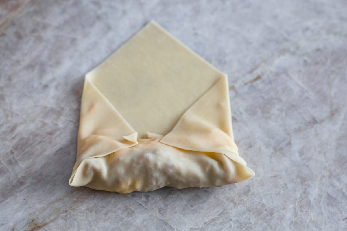 Overhead shot of a partially wrapped egg roll paper with ingredients inside. 