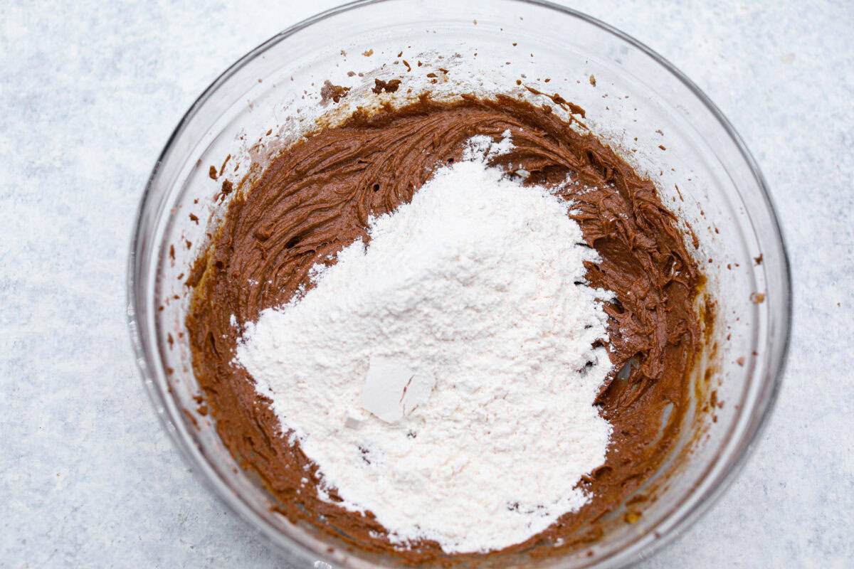 A bowl of chocolate pudding cookie dough with flour being added.