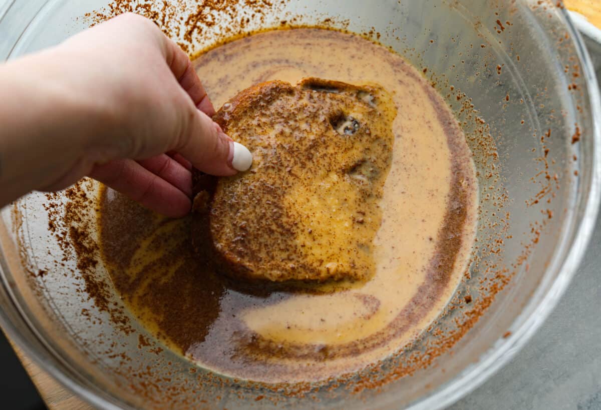 Dredging a slice of bread in the egg mixture.