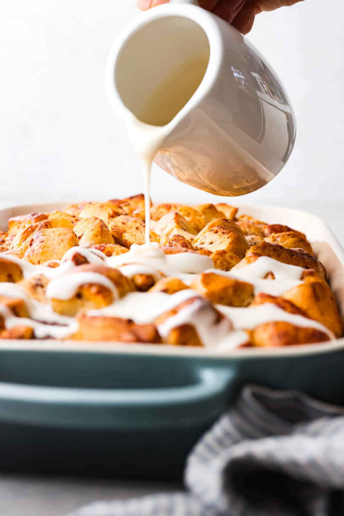 Icing being drizzled over baked cinnamon roll casserole. 