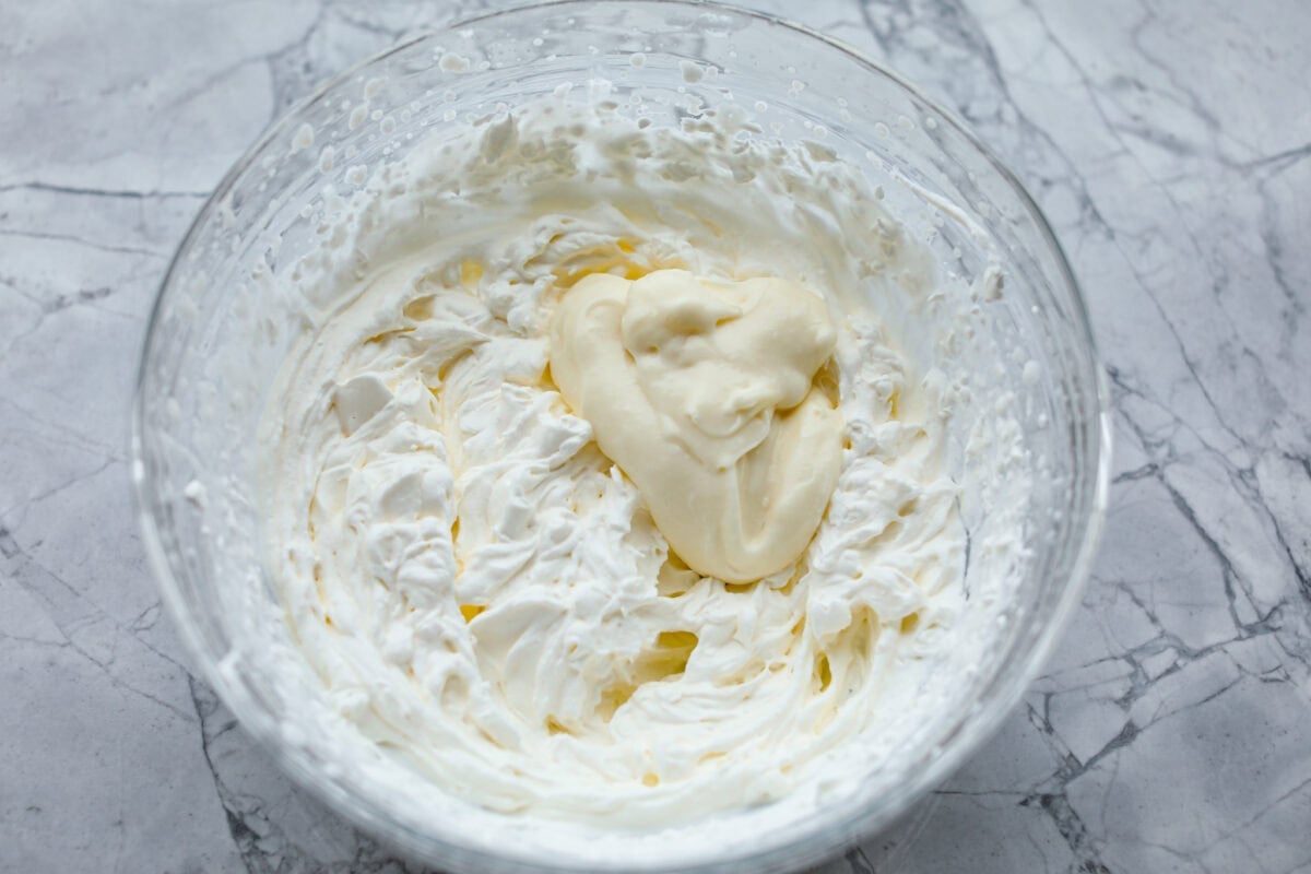 Overhead shot of a dollop of cream cheese mixture in the whipped cream in glass bowl. 