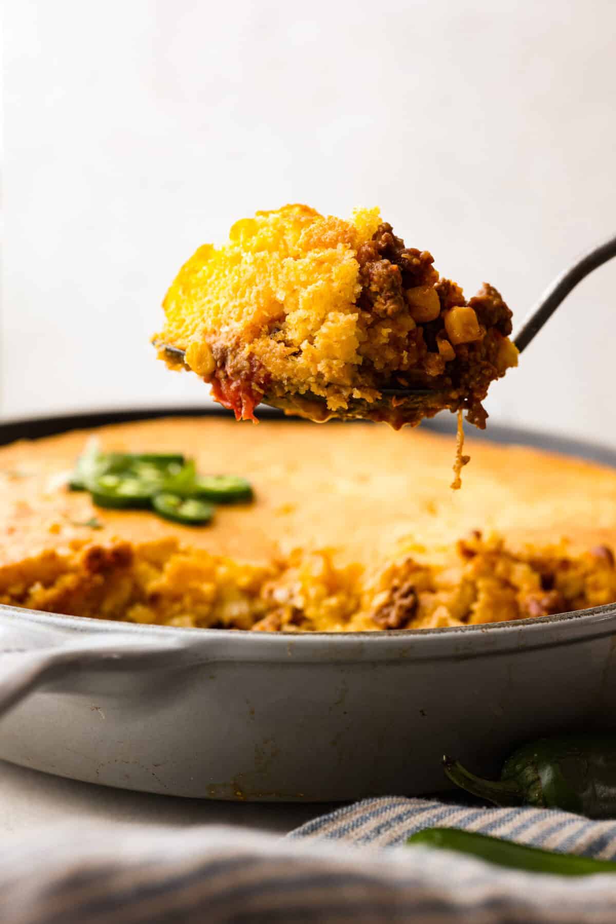 Side shot of a spoon holding a scoop of cowboy cornbread casserole above the whole dish. 