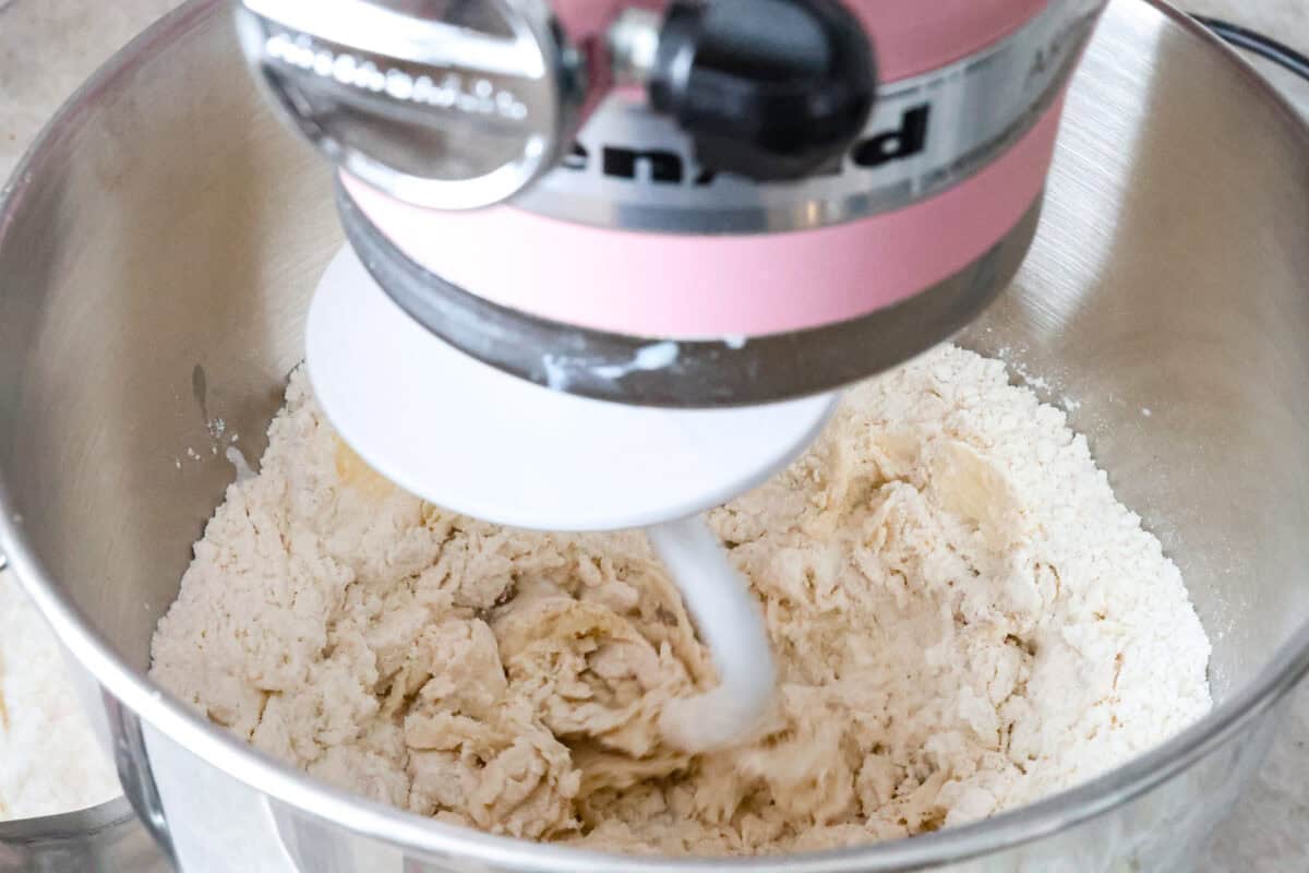 Angle shot of yeast mixture being mixed with butter and flour with dough hook in stand mixer. 