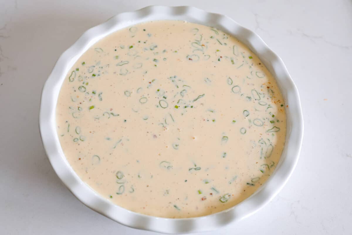 Adding the quiche mixture into a metal pan.