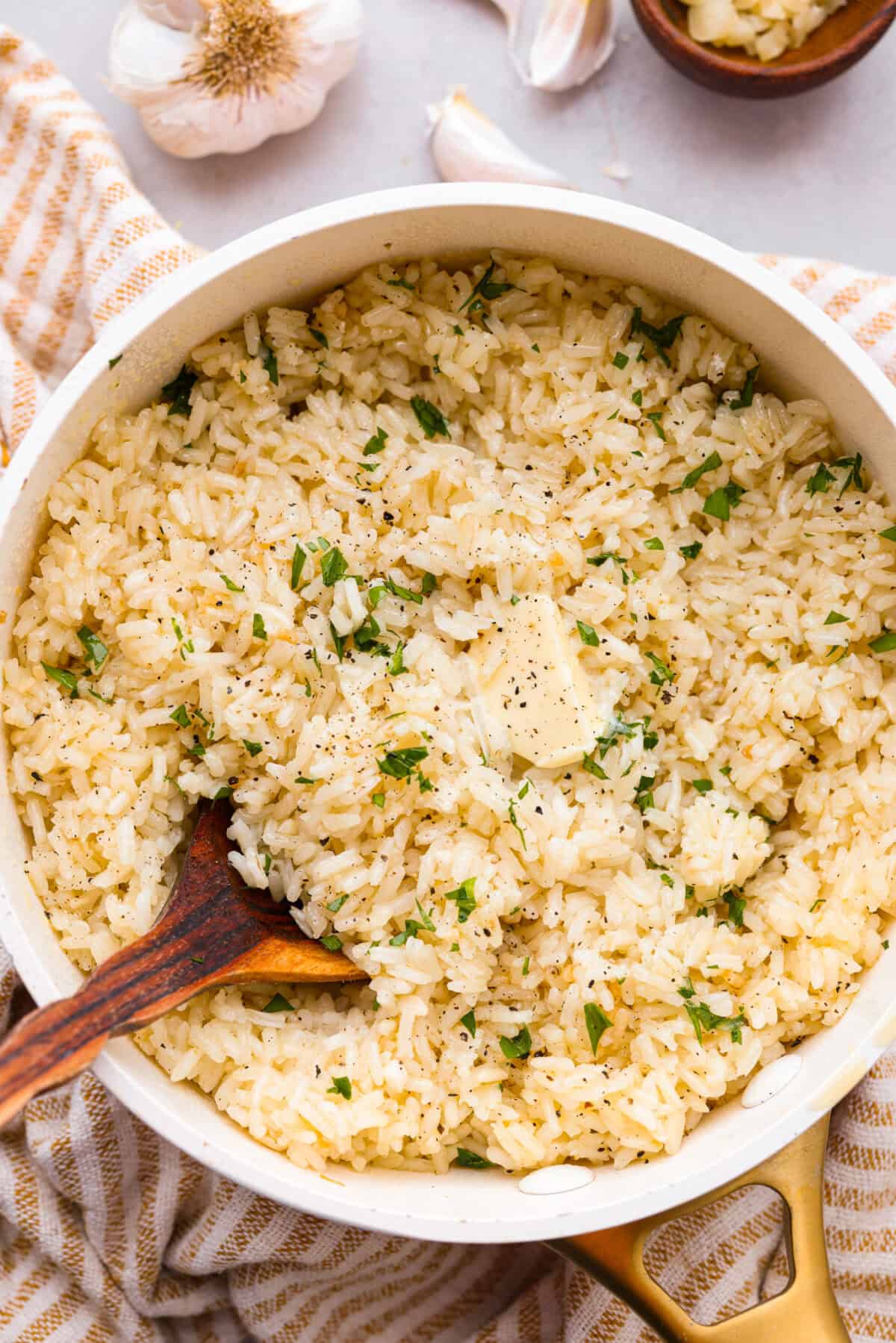 Overhead shot of garlic butter rice in a pot with wooden spoon, garnished with parsley. 