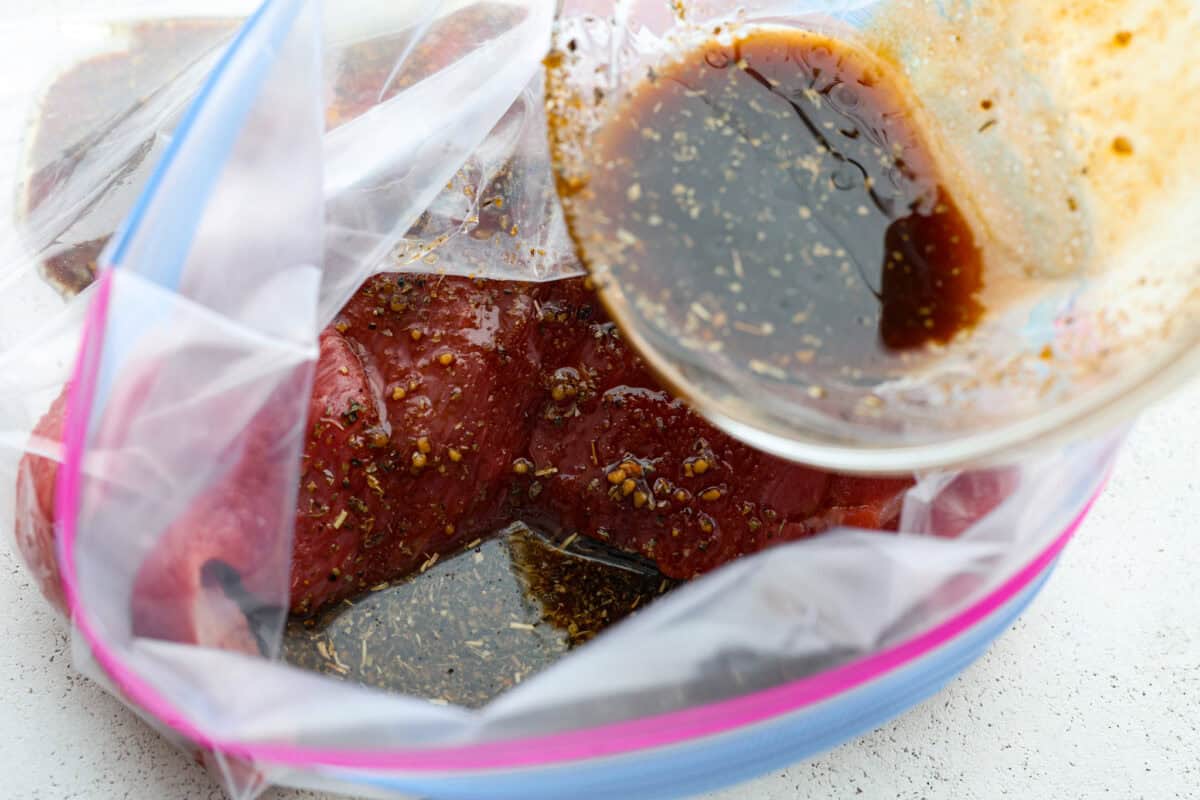 Close up shot of raw tri-tip in large zip-loc with marinade being poured over it. 