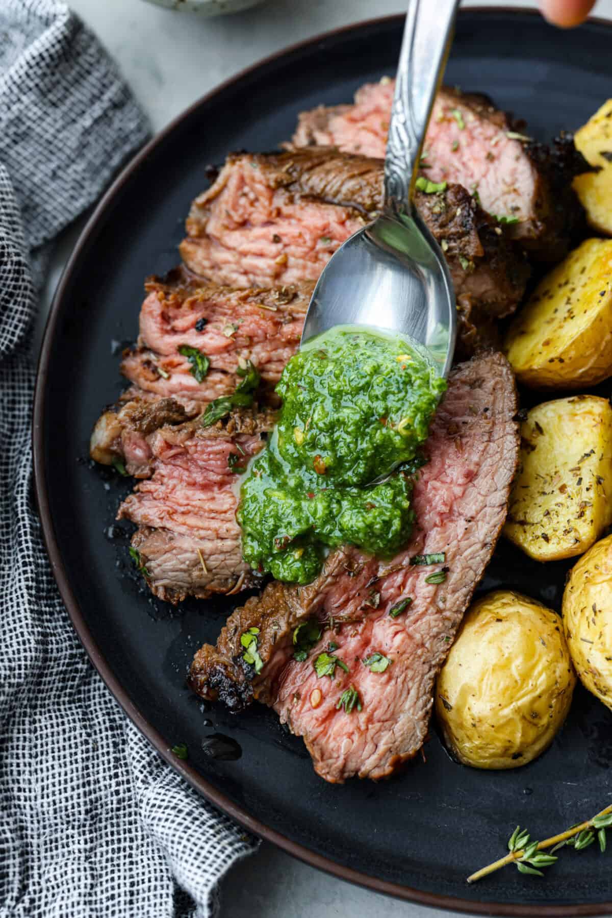 Overhead shot of chimichurri sauce being poured over slices of meat on a plate. 