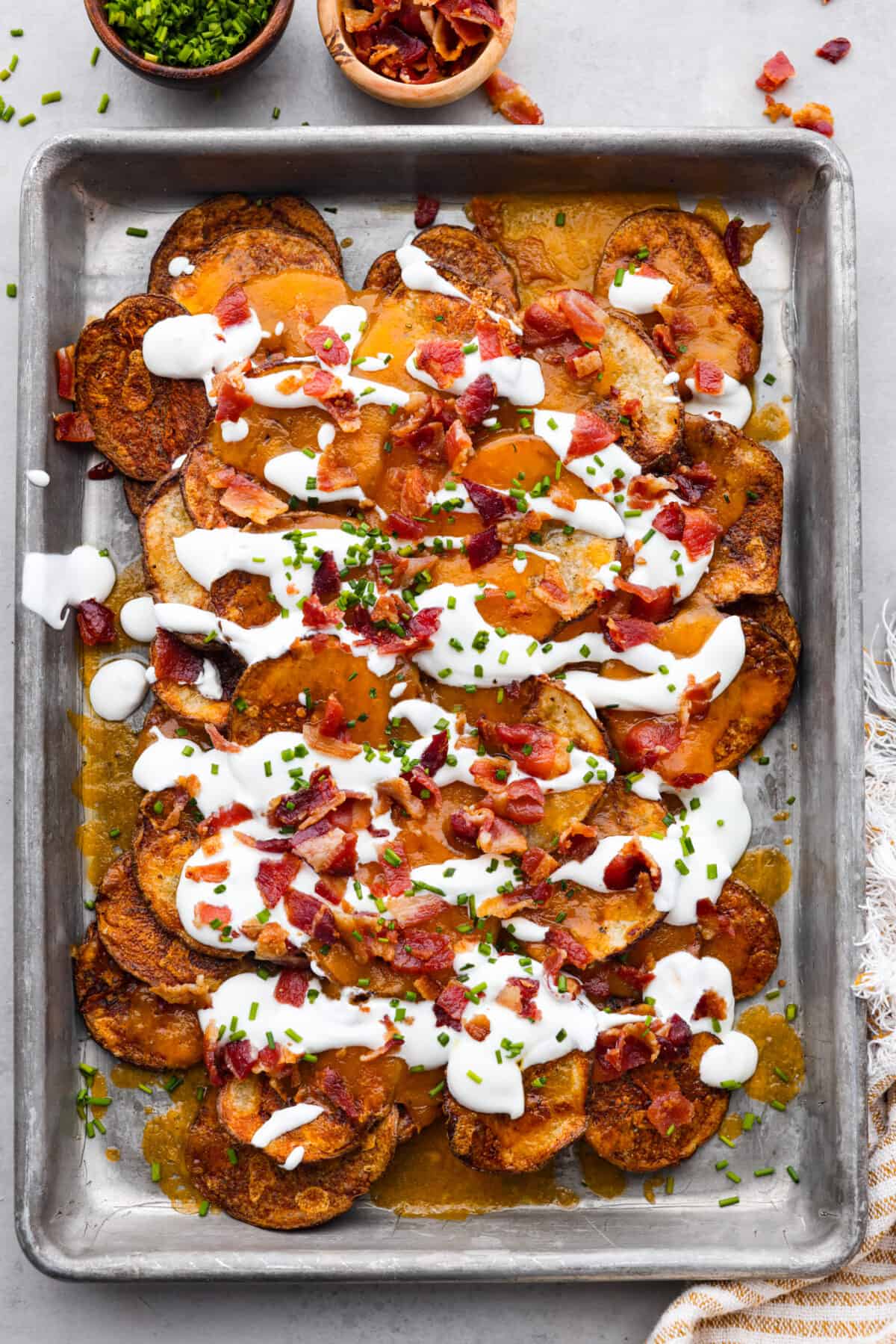 Top-down view of russet potato slices topped with bacon, chives, and sour cream.