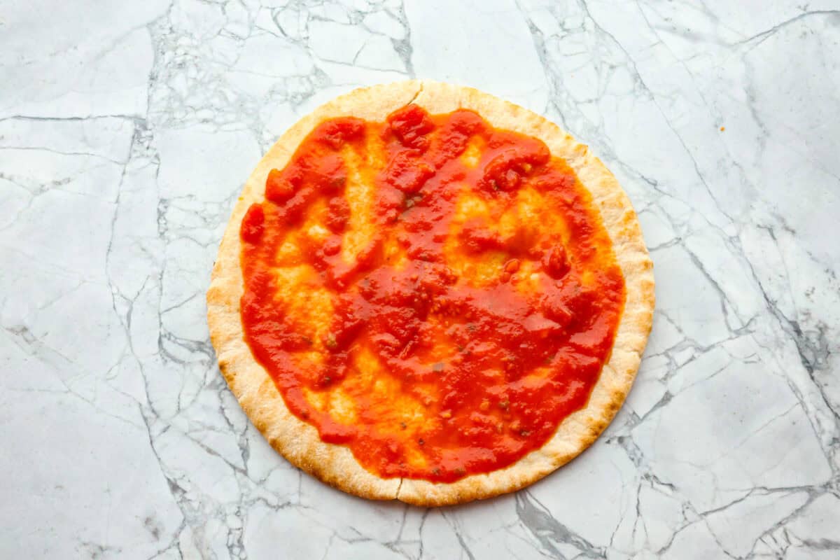 Overhead shot of pita bread with marinara sauce spread out on it. 