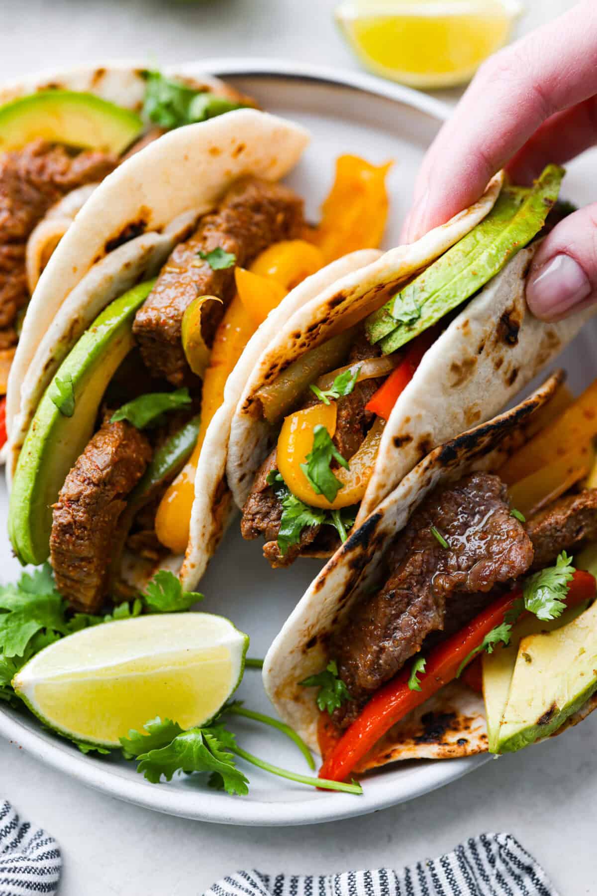 Angel shot of someone picking up a tortilla filled with fajita mix and topped with avocado. 