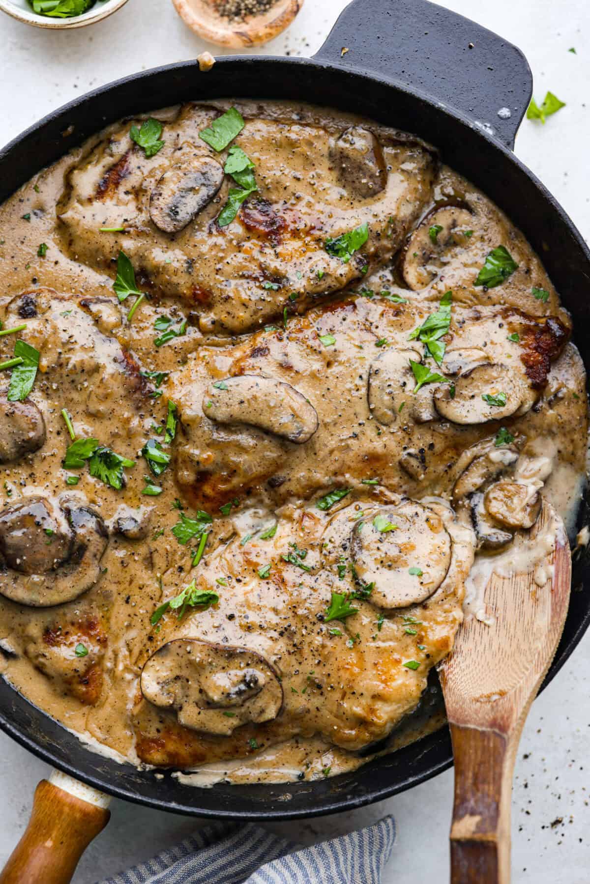 Overhead shot of skillet filled with smothered chicken with wooden spoon sticking out. 