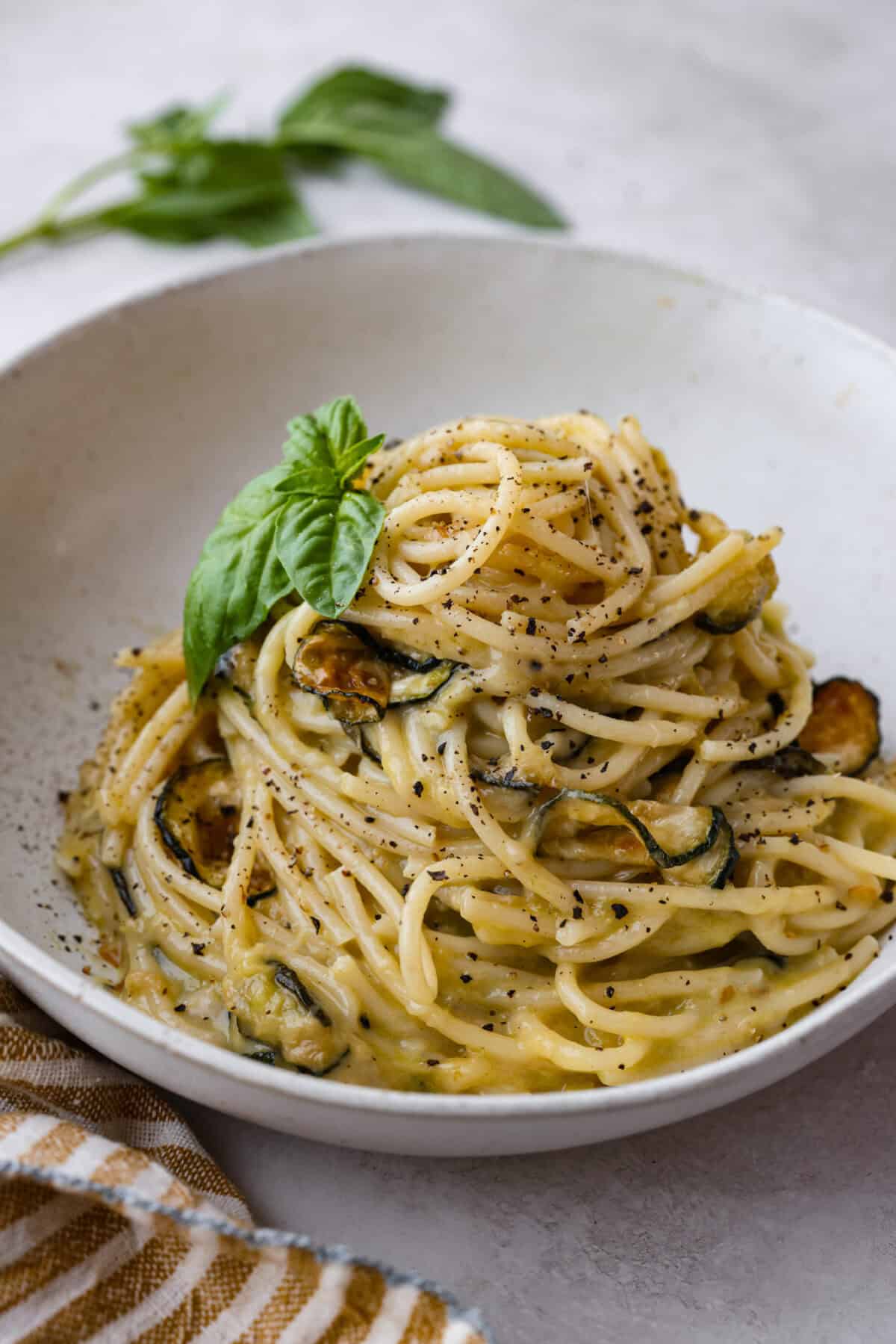 Close view of a pile of spaghetti alla Nerano in a white bowl garnished with fresh basil.