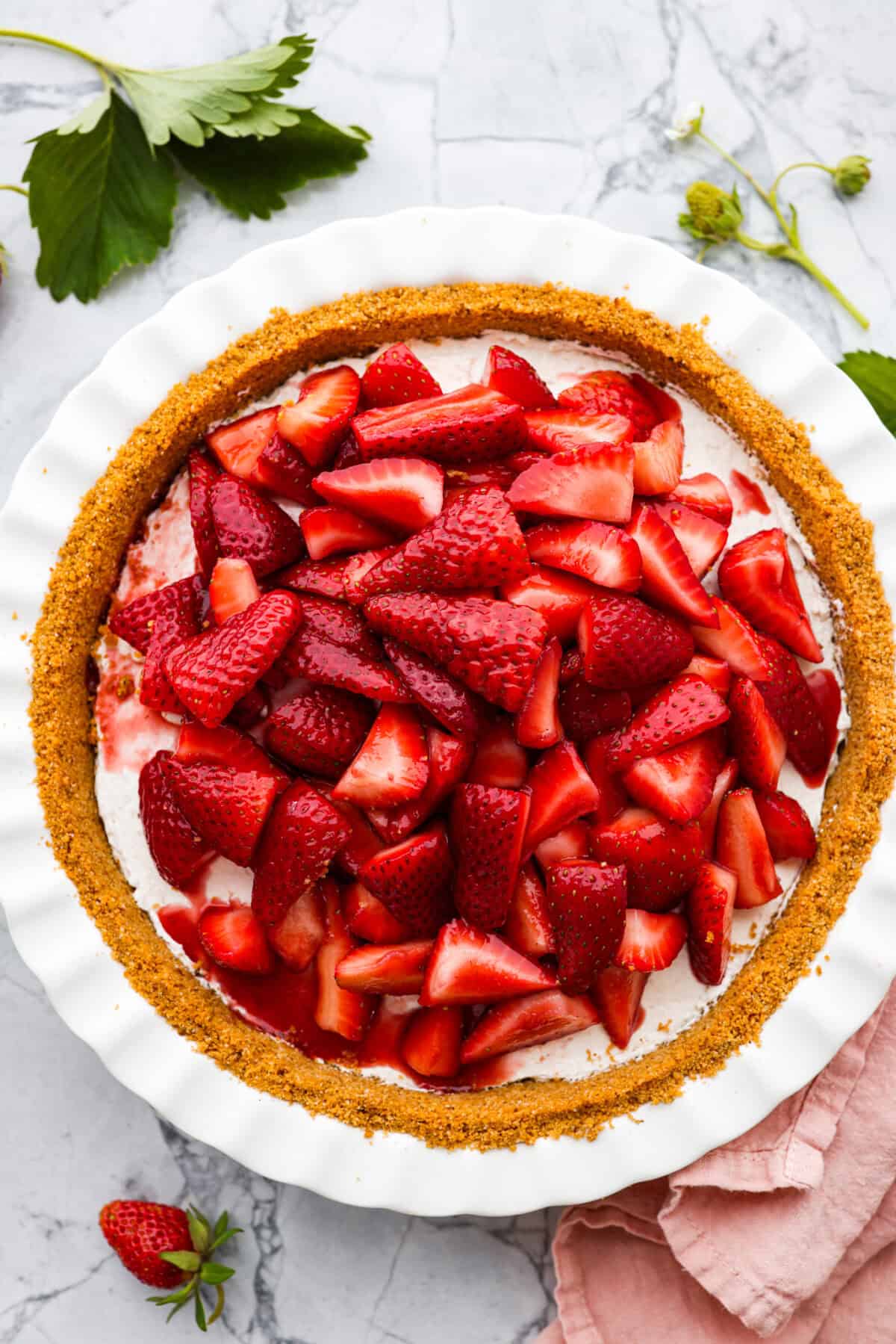 Overhead view of strawberry cream cheese pie, in whit pie pan on marble countertop. 