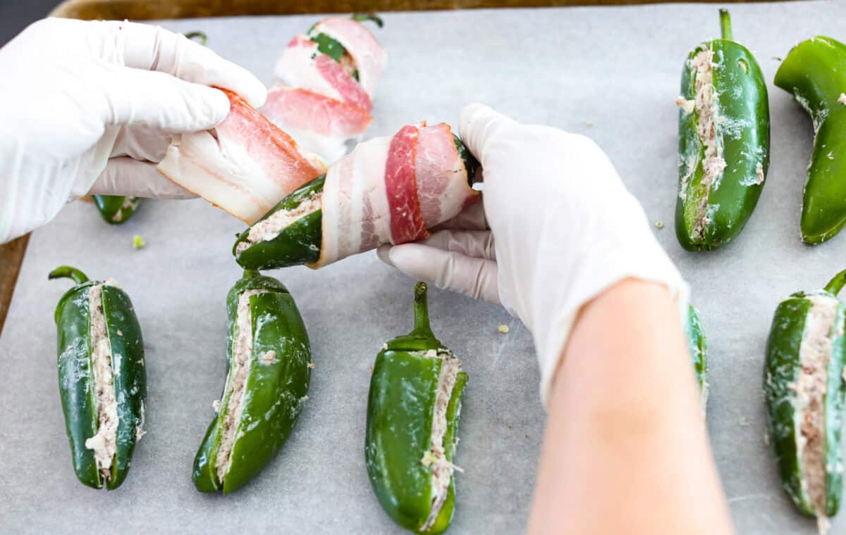 Overhead shot of someone wrapping stuffed peppers with bacon. 