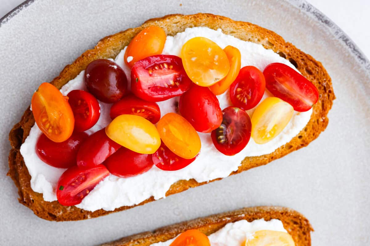 Overhead shot of toasted bread with ricotta and sliced tomatoes on top.