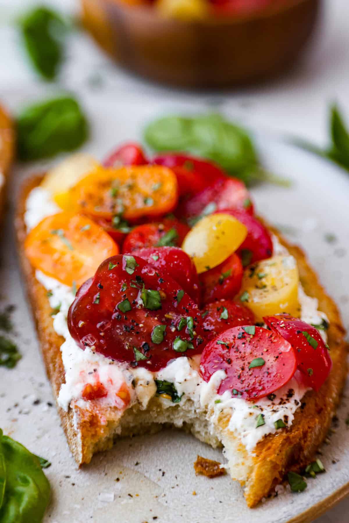 Angle close up of plated tomato toast with a bite taken out of it. 