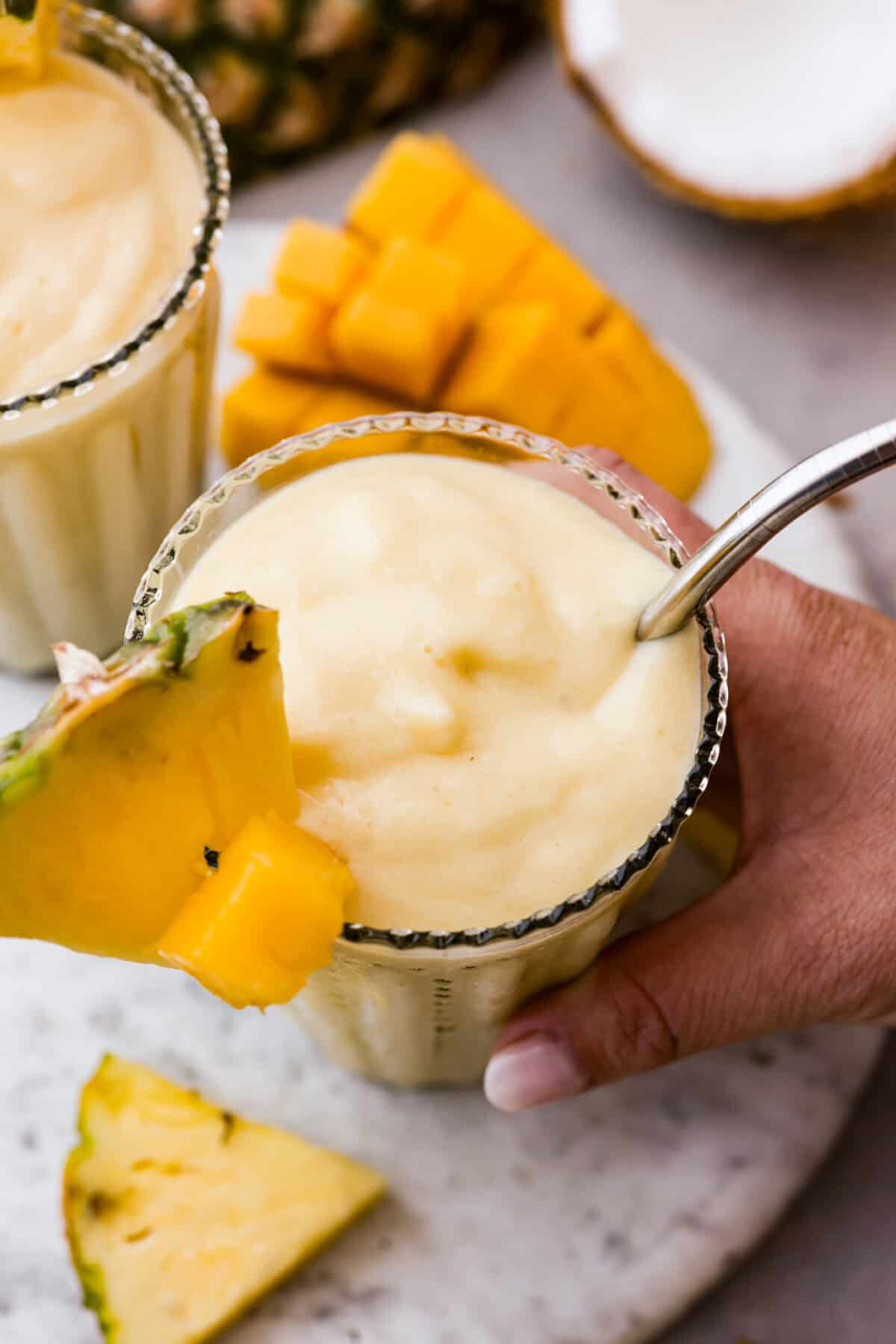 Angle shot of someone picking up the glass of tropical smoothie with wedge of pineapple in it. 