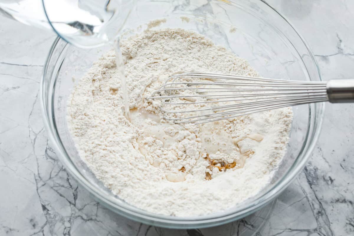 Overhead shot of glass bowl with mixed dry ingredients with wet ingredients being poured in. 