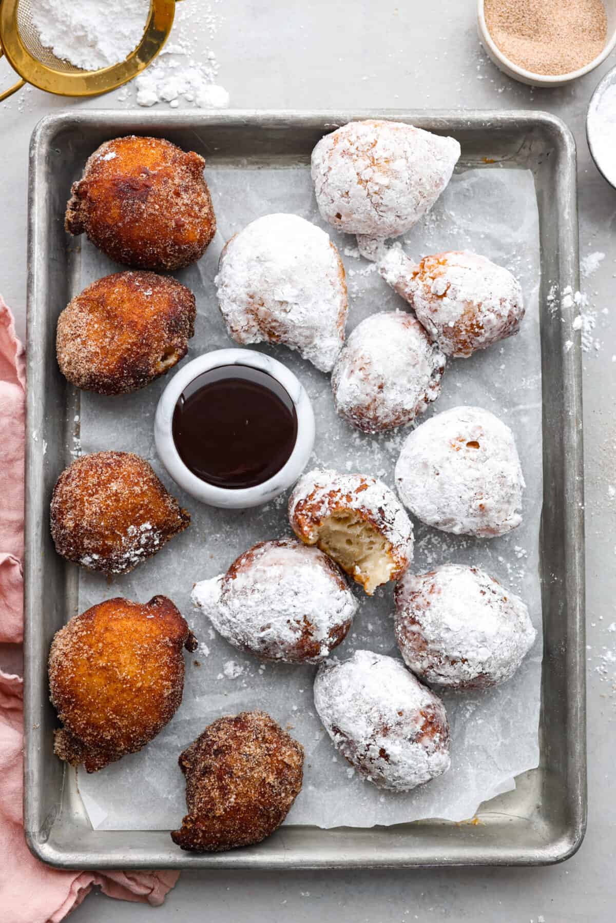 Overhead shot of a pan of italian donuts. Some are coated in powdered sugar and others in cinnamon and sugar. 