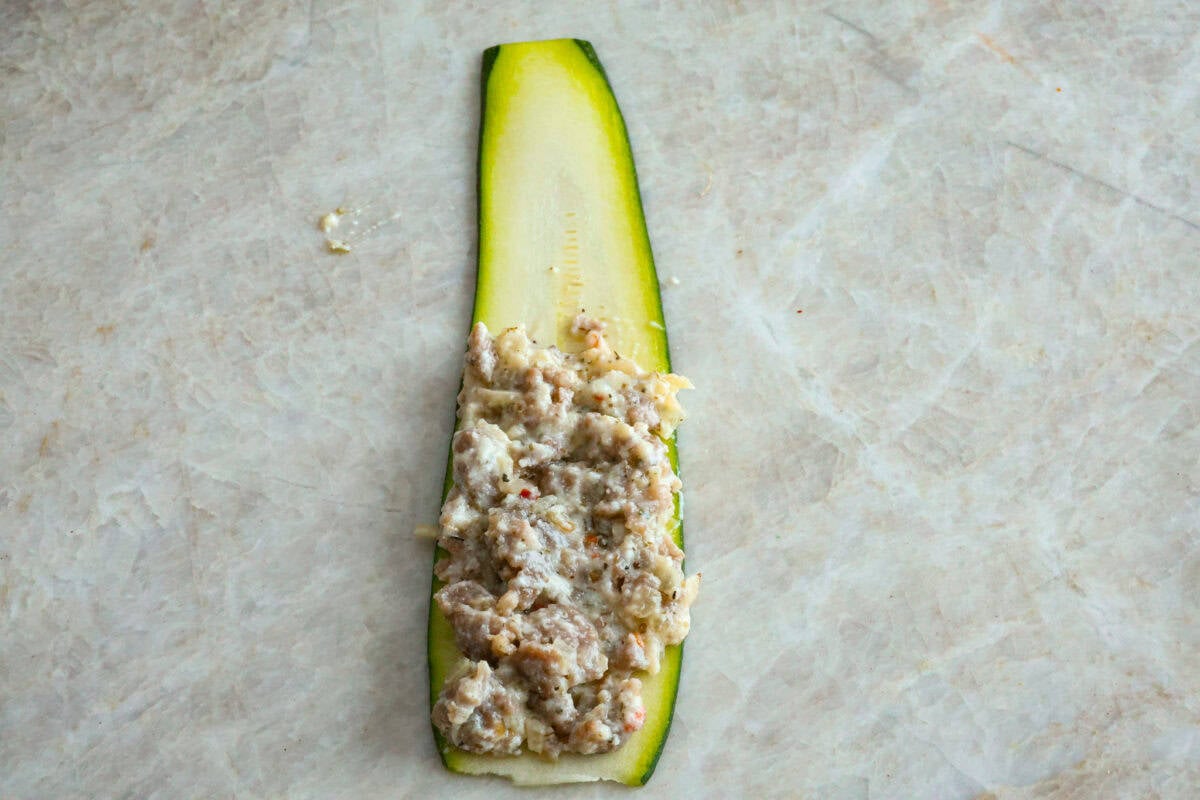 Overhead shot of zucchini ribbon with sausage and cheese mixture on one half. 