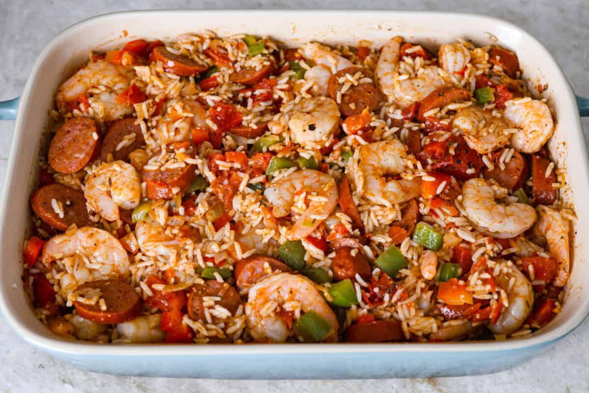 Overhead shot of shrimp sausage and veggies mixed with rice, tomatoes, and seasonings in a baking dish.