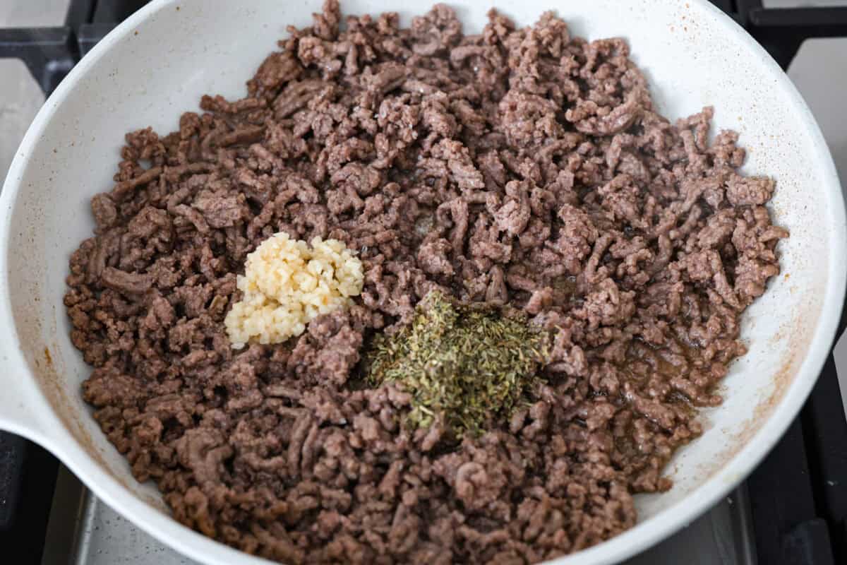 Overhead shot of browned beef with garlic and Italian seasoning in a skillet. 