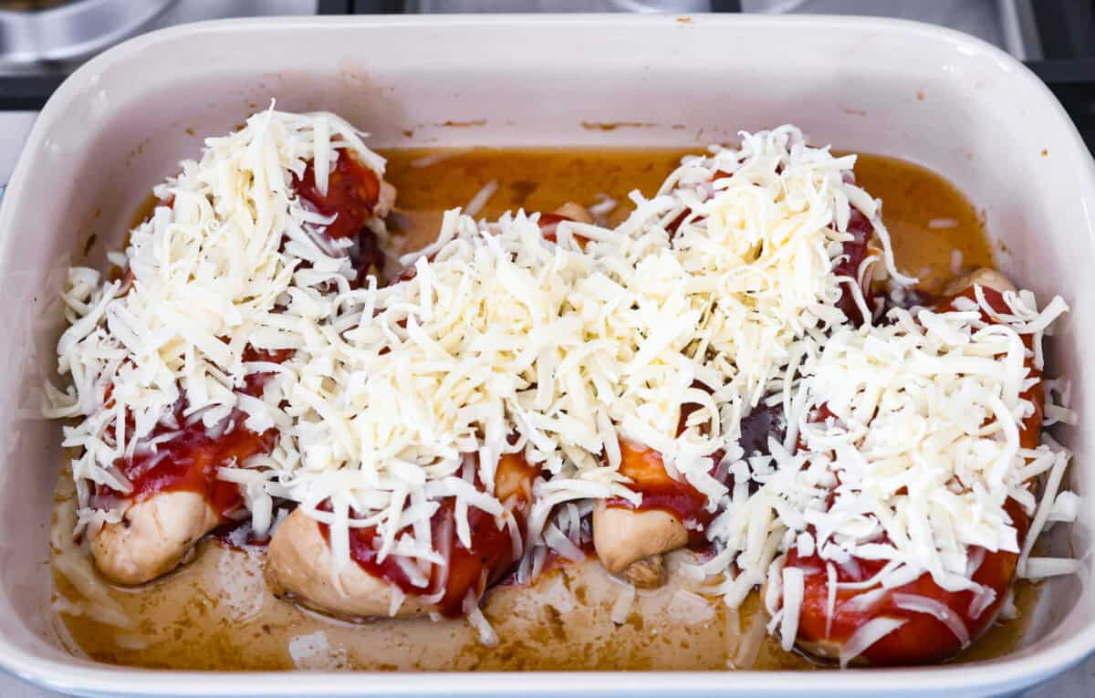 Overhead shot of a baking dish with chicken breasts with BBQ sauce and cheese spread on top. 