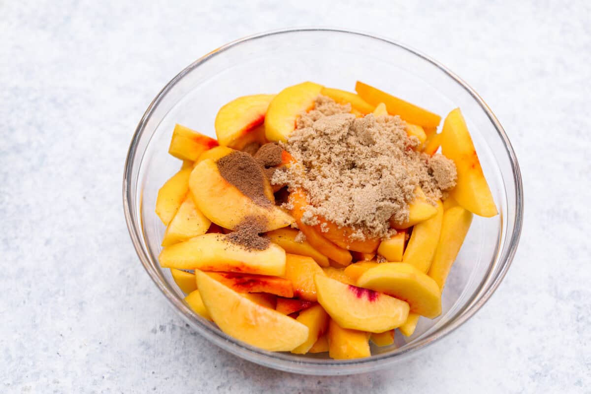 Overhead shot of a bowl of sliced peaches with brown sugar, cinnamon and nutmeg on top. 