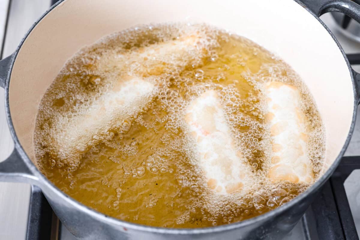 Overhead shot of egg rolls being fried in oil. 