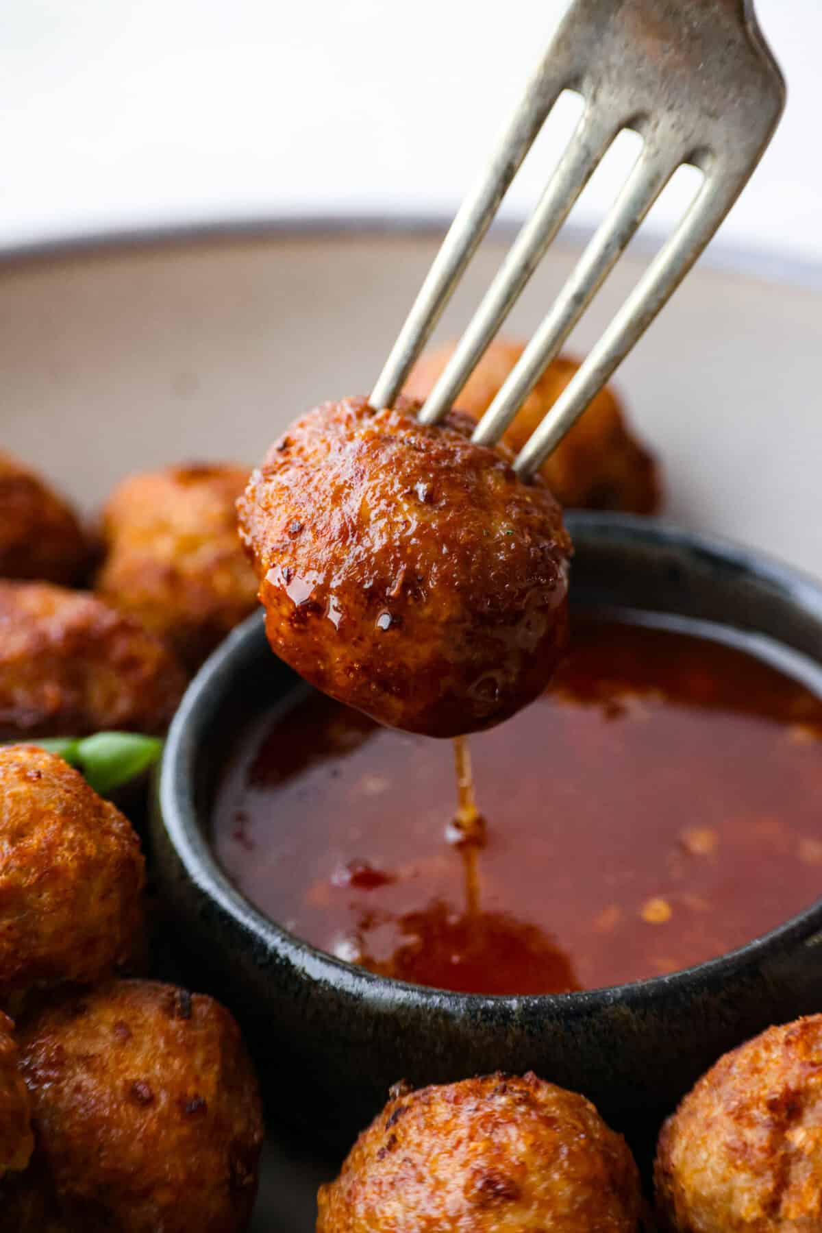 Close view of a fork dipping a meatball into a bowl of sweet chili sauce.