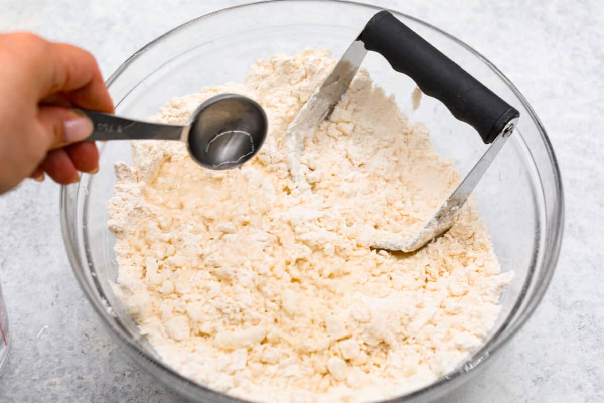 Angle shot of someone pouring tablespoons of water into the mixing bowl with flour and salt and shortening, 