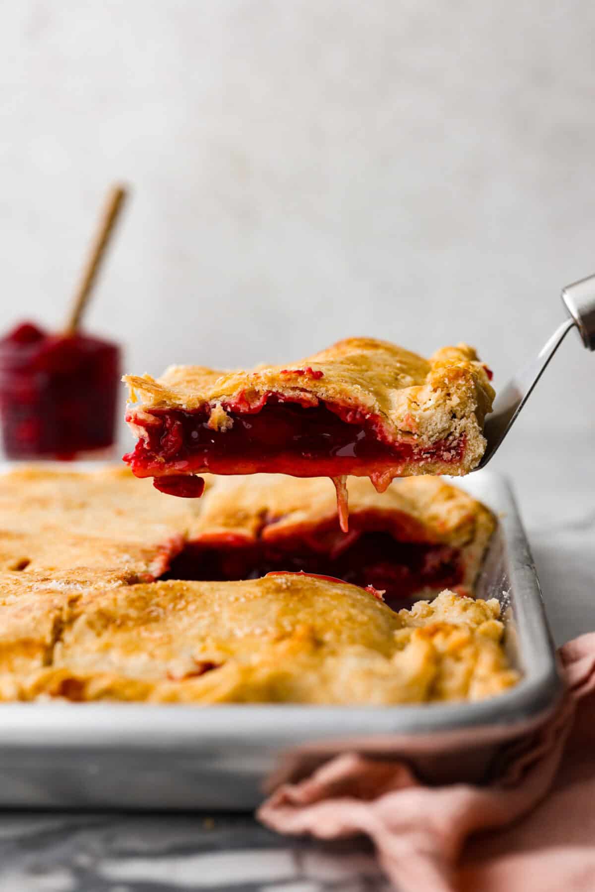 Side shot of a slice of cherry slab pie on a spatula being lifted out of the sheet pan. 