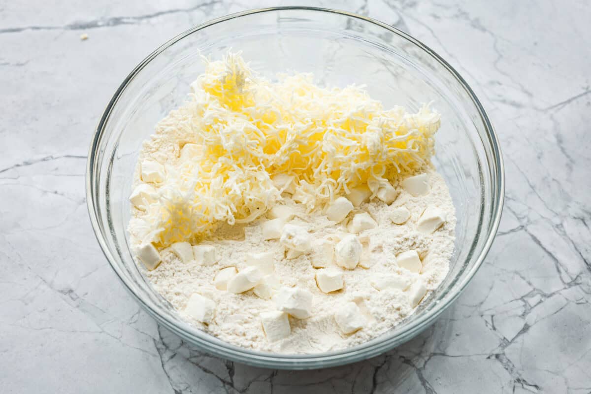 Overhead shot of flour mixture with shredded butter and cubes of cream cheese in a bowl. 