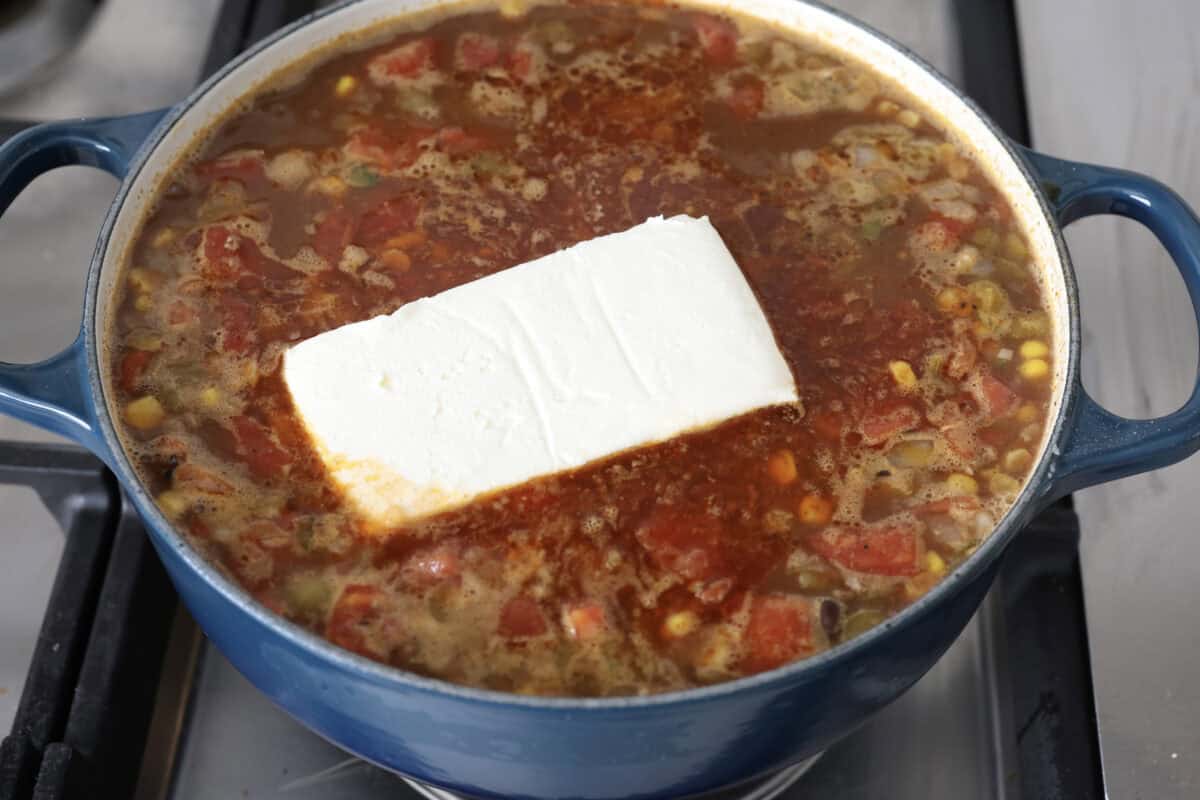 Angle shot of the soup mixture with a block of cream cheese added in the middle. 