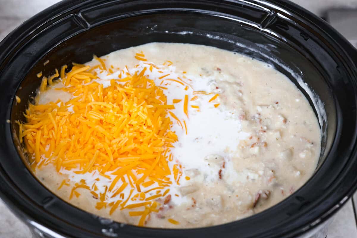 Overhead shot of cheese and half and half on top of mixed soup in crock pot. 