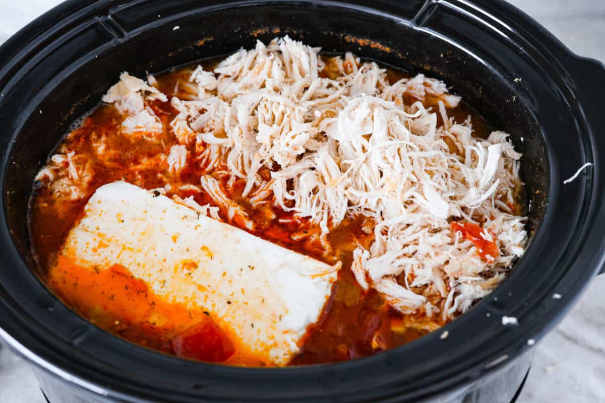 Overhead shot of shredded chicken and cream cheese added back to the crockpot. 