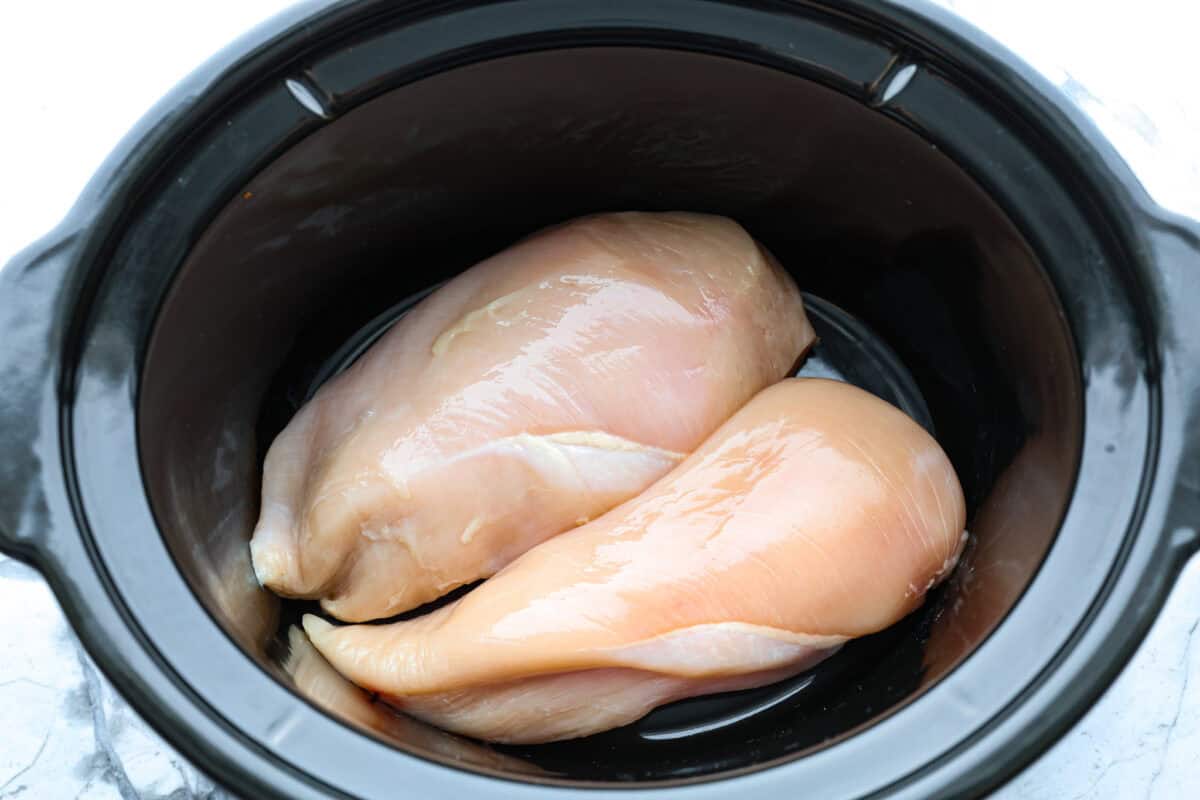 Overhead shot of raw chicken in the bottom of the crockpot. 