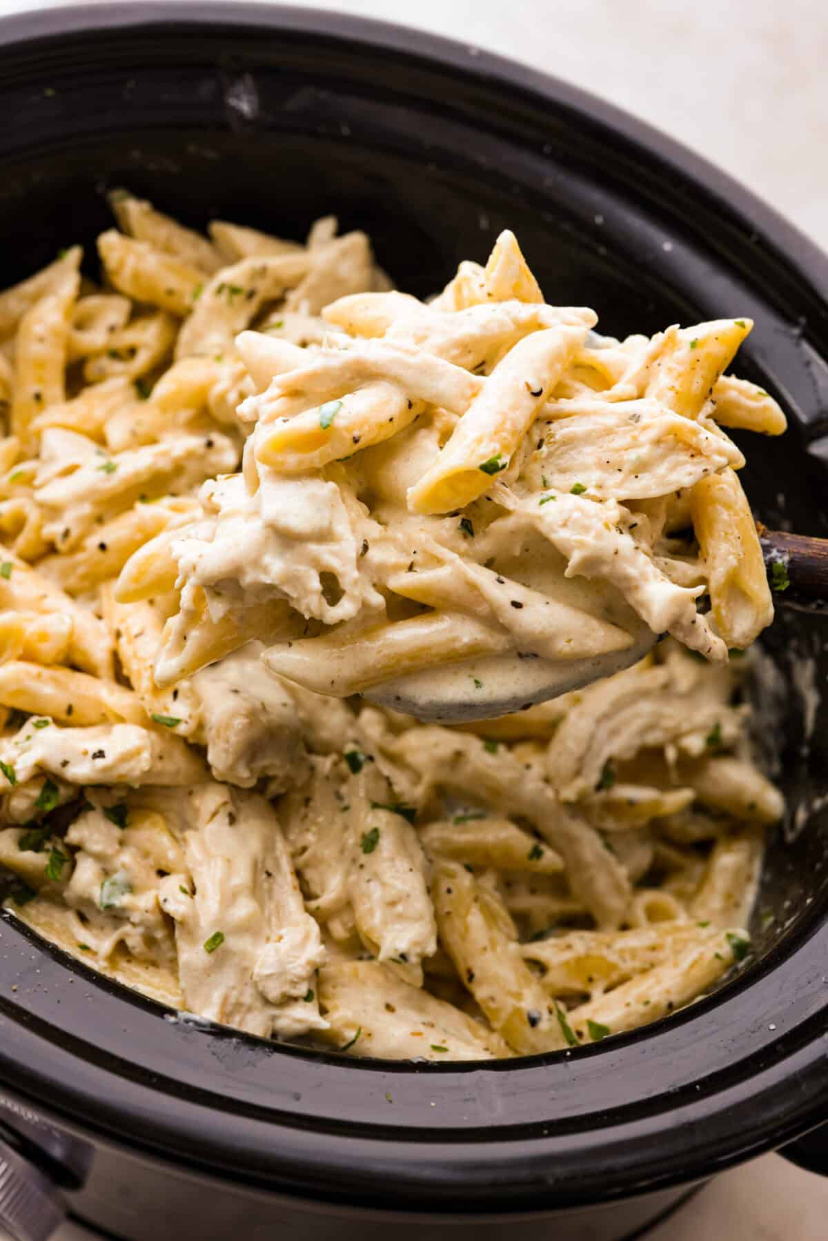 Close up shot of a scoop of crockpot chicken alfredo being scooped out of the crockpot. 