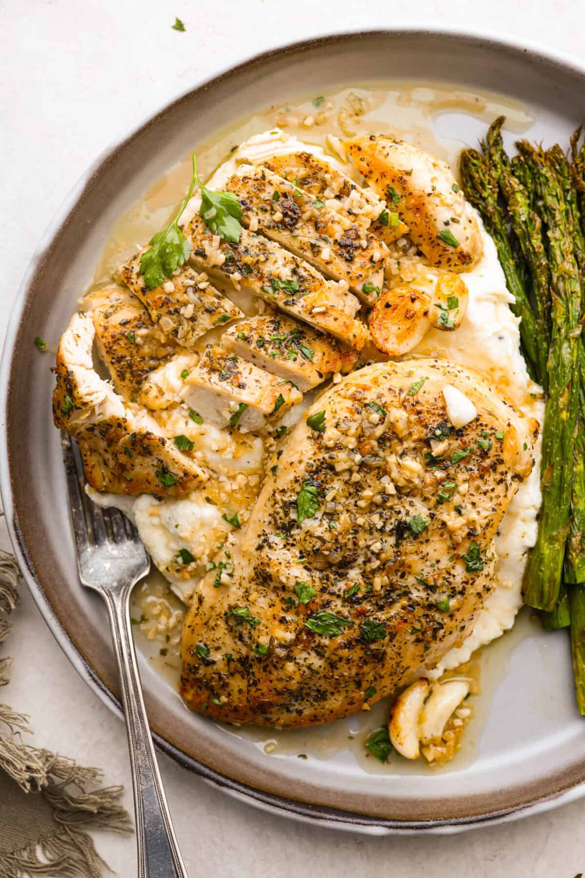 Overhead shot of plated garlic butter chicken over mashed potatoes next to asparagus. 