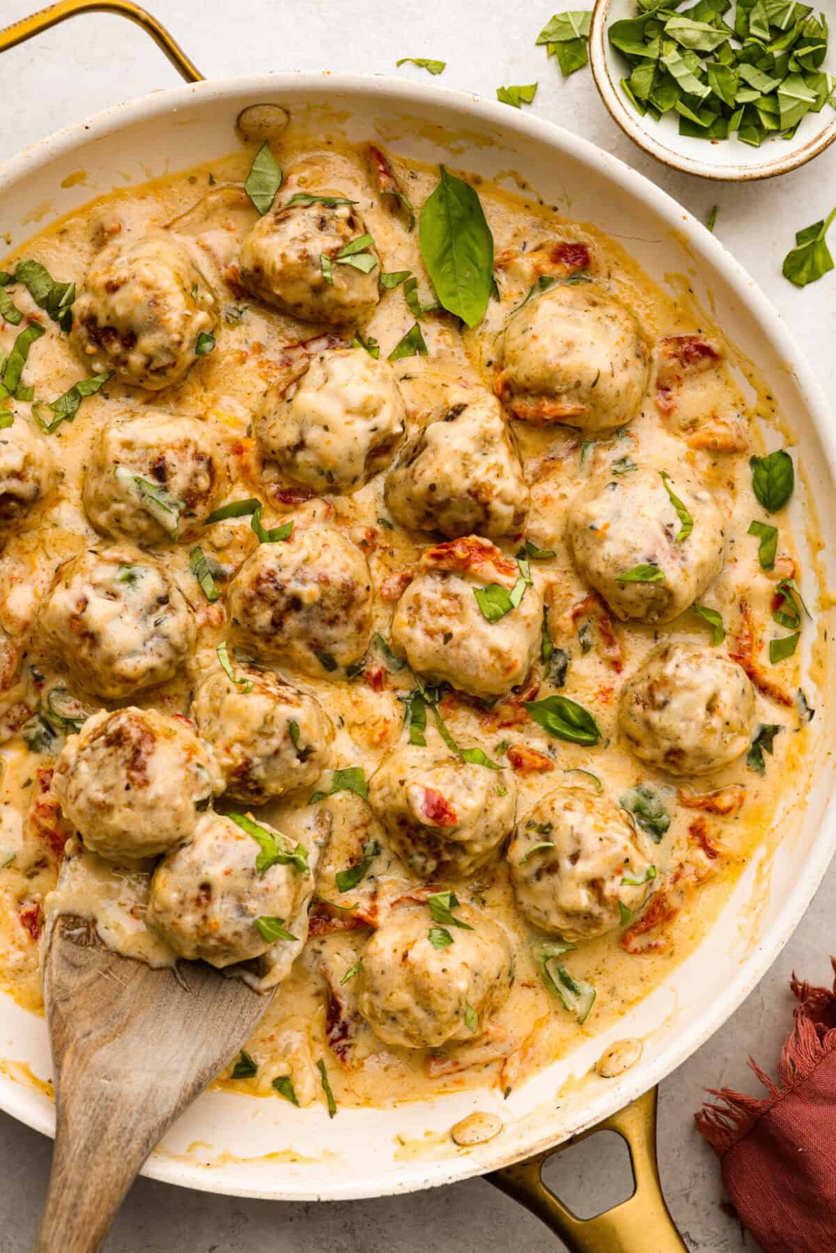 Overhead shot of marry me meatballs in a skillet with wooden spoon. 