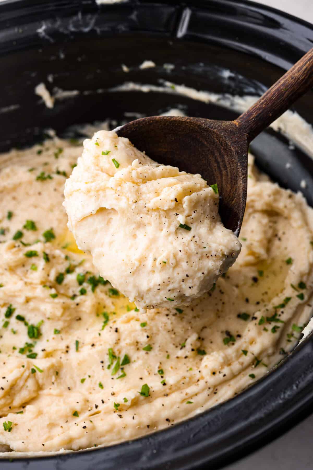 Close up shot of someone scooping a serving of million dollar mashed potatoes out of the crock pot. 