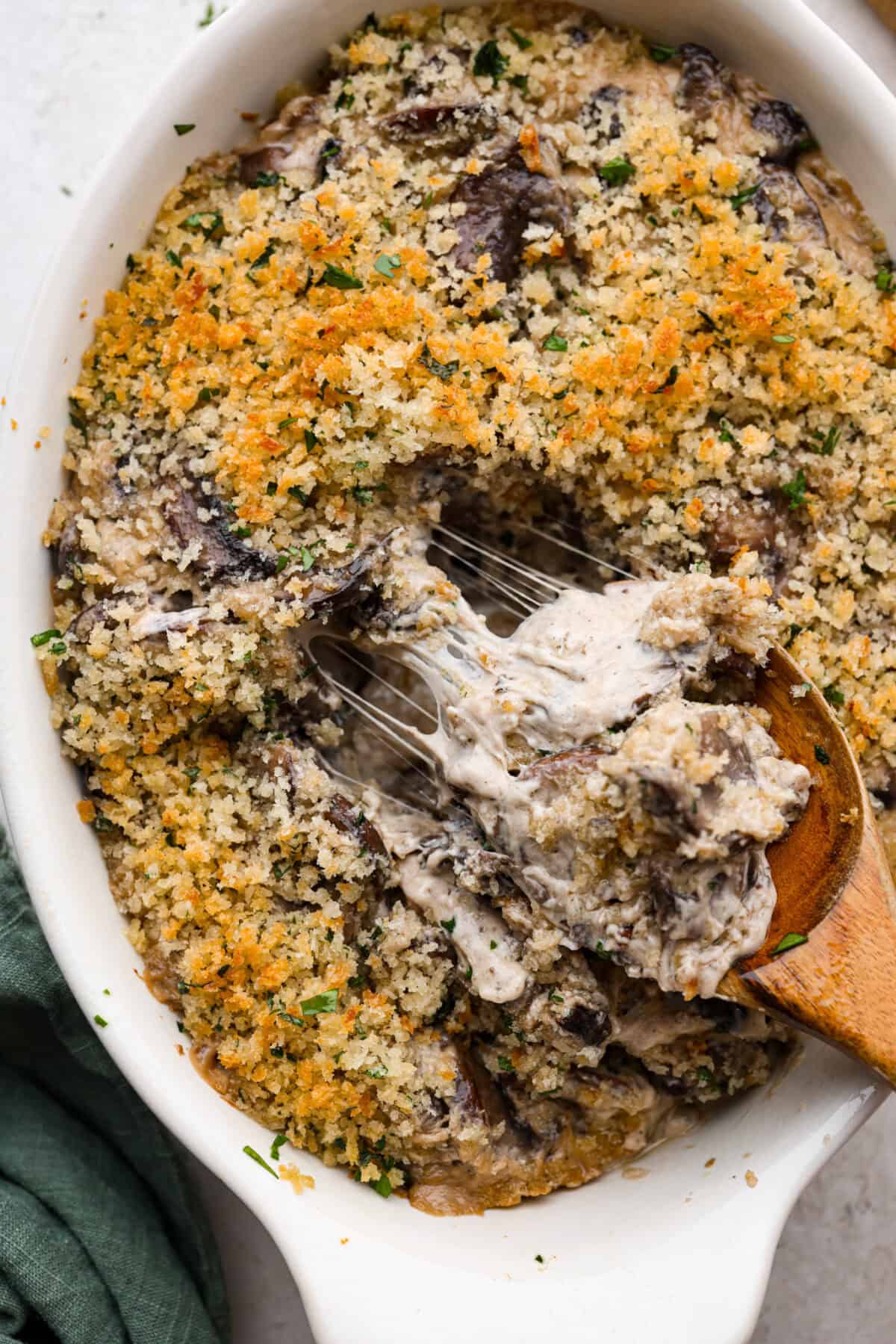 Close view of a spoon lifting up a cheesy spoonful of mushroom casserole.