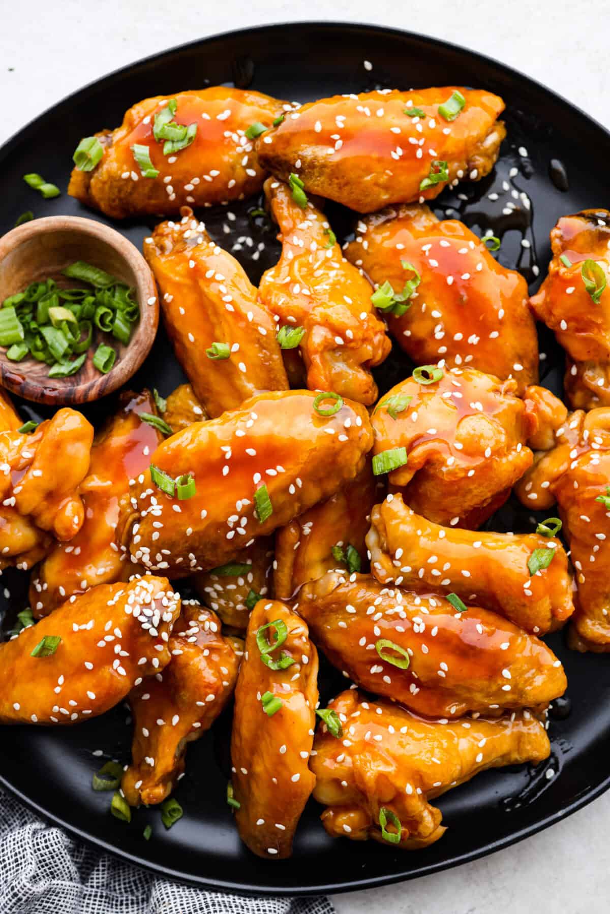 Overhead shot of a platter of sweet and sour wings garnished with chopped green onion and sesame seeds. 