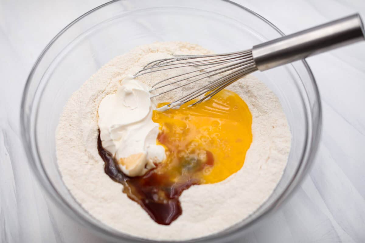 Overhead shot of sour cream, eggs, vanilla baking powder and salt being whisked in with the dry ingredients. 