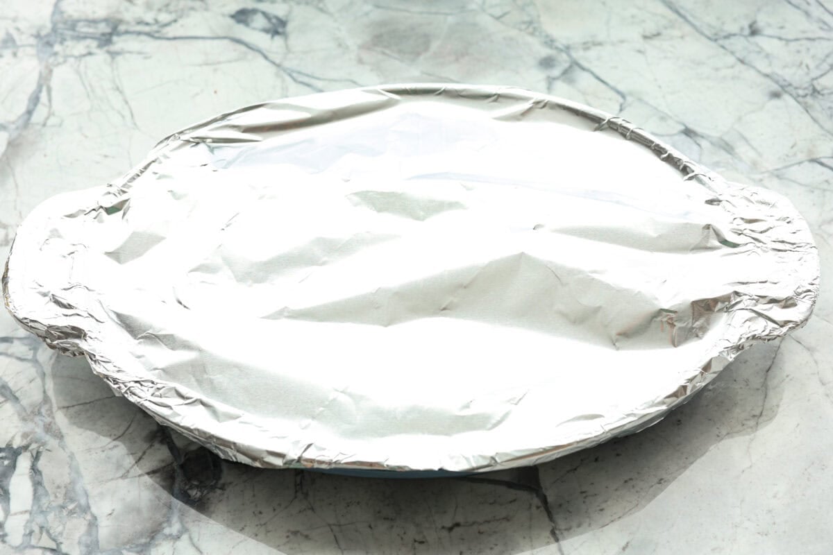 Overhead shot of baking dish with yams and sauce covered with tinfoil. 