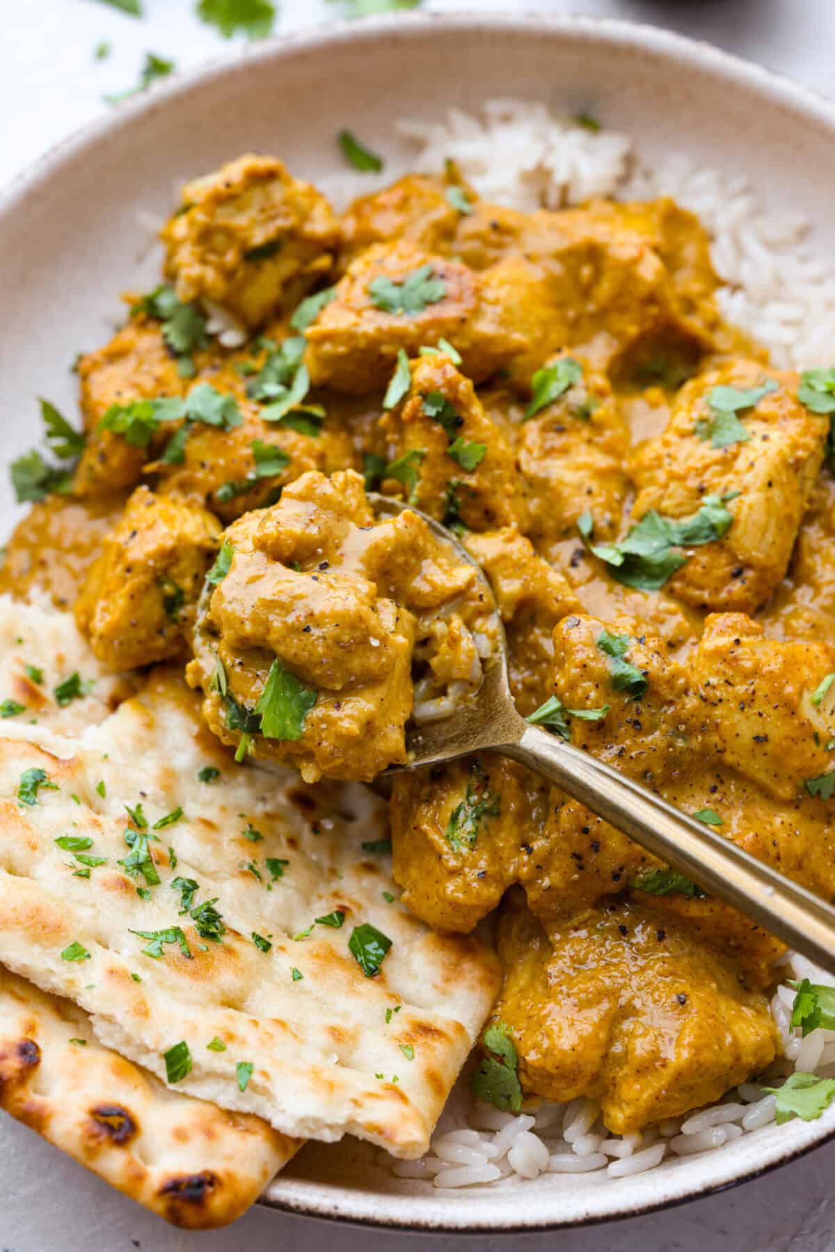 Close up shot of plated chicken korma with a bite on a gold spoon. 