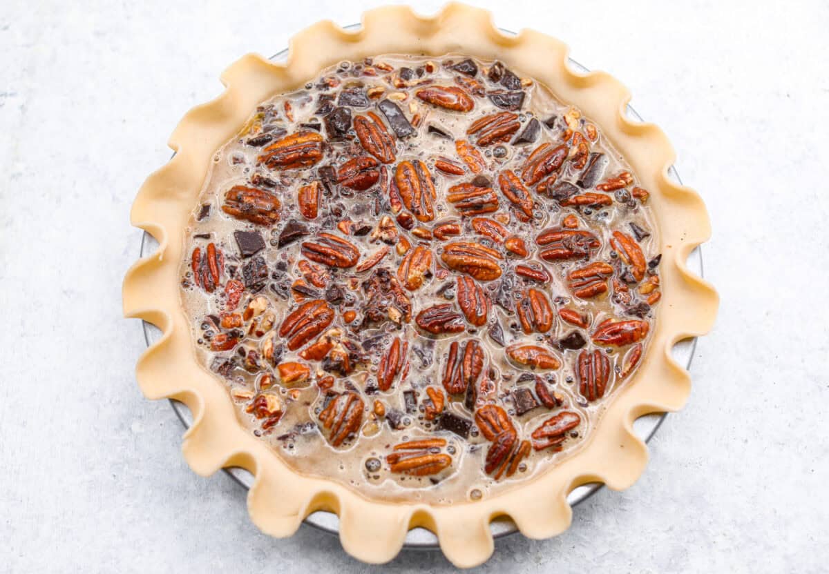 Overhead shot of the pie crust with pecans, chocolate and filling inside ready to go in the oven. 