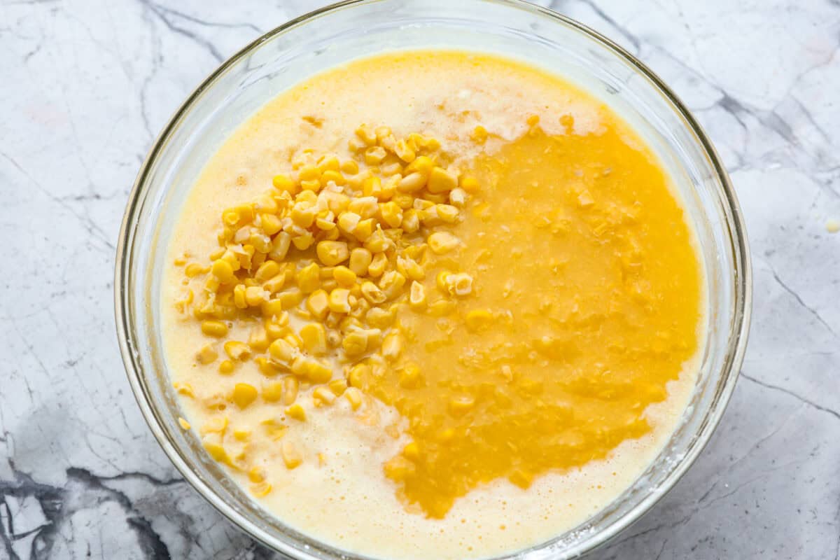 Overhead shot of egg and cornstarch mixture with corn, creamed corn, butter, and heavy cream in a glass bowl. 